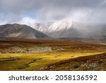 Autumn tundra and cold river on the background of misty snow-capped mountains