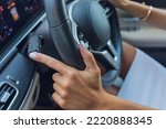 Woman's hand switches the lobes of the gear selector on the steering wheel. Hand is switching car gear lever, close up shot of a manual gear changing paddle on a car's steering wheel.