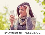 Annoyed upset woman in glasses looking at her smart phone with frustration while walking on a street on an autumn day  