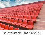 Stands for fans and spectators on an open football field. Plastic seats for spectators in a sports complex. Red benches for spectators at the stadium. Rows of plastic chairs. Gomel. The stadium 