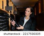Woman in the wine cellar with bottles in background drinking and tasting wine.