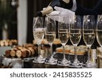 The waiter pouring white sparkling wine. Catering service concept. Barmen pours champagne into flute glasses. Champaign is being poured into glasses. Bottle in a closeup view. Rows of full glasses.