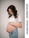 Small photo of Female waiting for newborn baby on white background. Young pregnant girl touching and holding belly and caring about health indoors. Pregnancy motherhood procreation concept. Belly of a pregnant woman