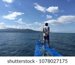 Small photo of Negros Oriental, Philippines; April 21, 2018: A Filipino deckhand stands at the bow of a small wooden boat travelling near the coast of Negros Island, looking for a good spot to the drop anchor.