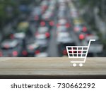 Shopping cart icon on wooden table over blur of rush hour with cars and road, Shop online concept