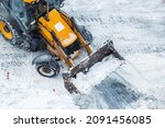 Small photo of Tractor loader machine uploading dirty snow into dump truck. Cleaning city street, removing snow and ice after heavy snowfalls and blizzard. Snowplow outdoors clean pavement sidewalk road driveway