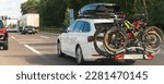 Small photo of Back view modern white family wagon car with mounted roof box trunk and bike tail carrier driving european highway road against blue sky summer day. Lifestyle travel adventure trip journey concept