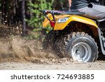 Small photo of An ATV quadbike get stuck in a sandy road near forest and having wheel-spin making a spray of sand.