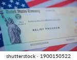 Blurred COVID-19 economic Stimulus American rescue program check on blurred USA flag and sun light background. Relief program concept. 