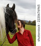 Small photo of A woman interacts with her skewbald Irish Gypsy Cob horse in a grassy field