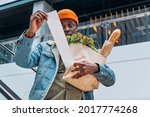Small photo of Doubting African-American person in denim jacket looks at sales paper receipt total holding pack with food products on escalator