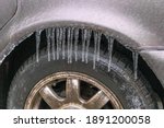 Close-up of an icy car body with icicles over the wheel close-up.