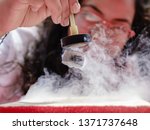 Small photo of Female Student Demonstrates Quantum Magnetic Levitation and Suspension Effect. A splash of liquid nitrogen cools a ceramic superconductor forcing it to float in air below a magnet