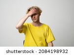 Small photo of Young man doing facepalm gesture. Portrait of ashamed abashed man in yellow t-shirt covering his face with hand on a white background. Copy space for advertising.