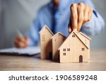 Small photo of Businessman choosing mini wood house model from model on wood table, Planning to buy property. concept of Choose the best.