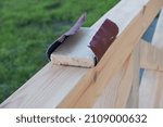 Small photo of Sanding wood. A male carpenter is sanding the wooden beams of a made gazebo. Hand of a Carpenter Rubbing Wood With Sand Paper