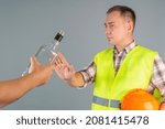 Small photo of A male construction worker in work clothes refuses a proffered bottle of strong alcohol. Refusal to drink at work