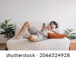 Small photo of Bored Asian man relaxed and use smartphone for killing time alone in apartment.