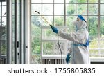 Small photo of worker from decontamination services wearing personal protective equipment or ppe including suit, face shield and mask. He uses disinfectant to spray and clean scientist lab