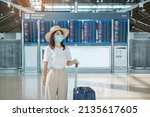 Small photo of Young female wearing face mask with luggage walking in airport, protection Coronavirus disease infection, Asian woman traveler with hat. Time to travel, Test and Go and vaccine booster dose concept