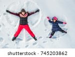 Happy family, mother and cute daughter making snow angel while lying on snow. 