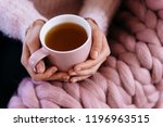 Soft cozy photo of woman in warm pink sweater holding cup of hot tea. Giant, large warm merino wool plaid blanket. Fall or winter time concept. The girl in a soft knitted sweater drinking tea 