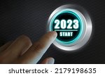 Small photo of Finger about to press a car ignition button with the text 2023 start. Year two thousand and twenty three concept. Composite image between a hand photography and a 3D background.