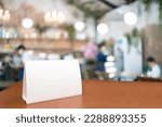 Small photo of Blank menu frame label mockup. Mock up menu frame on table in bar restaurant, stand for booklet with white sheet of acrylic tent card paper in blur cafeteria, cook chef in background.