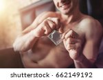 Cropped image of a smiling man holding condom in hand while lying on bed.