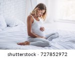 Attractive pregnant woman is sitting in bed and holding her belly. Last months of pregnancy.