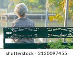 Asian elderly woman depressed and sad sitting back on bench in autumn park.