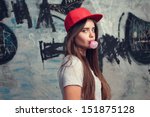 trendy beautiful long haired young model posing on graffiti background. Blow bubblegum. red cap. grey t-shirt.