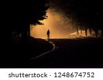 A person walk into the misty foggy road in a dramatic mystic scene with warm colors. Mysterious man walking in the mist