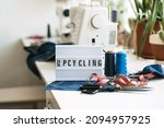 Small photo of Upcycling text on light board on sewing machines with old blue jeans background. Denim clothes, scissors, thread and sewing tools in sewing studio. Denim Upcycling and repair