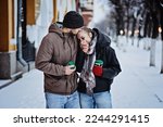Small photo of Winter Coating coldhearted dating trend. Winter Date Ideas to Cozy Up. Cold season dates for couples in love. Young couple with coffee walking, hugging and kissing in winter city street