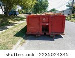 End view of a large red beat up dumpster on the street by a curb in a residential development