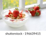 Crunchy musli (whole grain oats) served with fresh strawberries and low fat yogurt in a glass bowl - healthy breakfast on old farmhouse window sill