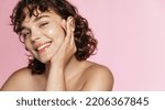 Small photo of Beautiful curly girl smiles as she likes skincare effect after beauty gel. Portrait of young woman washing her face and body, pink background.