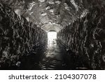 Small photo of An old culvert or storm drain tunnel with light in the end is built of stone, overgrown with cobwebs.