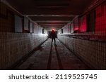 Silhouette of a man with a red lantern in dark interior of an abandoned underpass tunnel lit by a lantern.