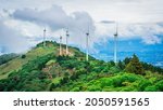 Wind turbines on top of a mountain on the background of a city. Beautiful green forest on the foreground.
