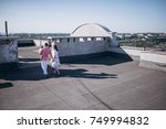 Small photo of Woman and man walking on the rooftop. They are holding hands each other. Man holds his little son on the hand. They enjoy morning sun and amazing view. They are wearing tricksy light summer clothes.