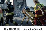Small photo of On the Car Crash Traffic Accident Scene: Paramedics and Firefighters Rescue Injured Victims Trapped in the Vehicle. Medics Use Stretchers, Perform First Aid. Firemen Grab Equipment from Fire Engine