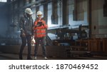 Small photo of Two Heavy Industry Engineers Walk in Steel Factory, Use Tablet and Discuss Work. Industrial Worker Uses Angle Grinder in the Background. Black African American Specialist Talks to Female Technician.