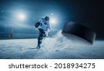 Ice Hockey Rink Arena: Professional Player Shooting the Puck with Hockey Stick. Focus on 3D Flying Puck with Blur Motion Effect. Dramatic Wide Shot, Cinematic Lighting.