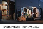 Small photo of Outside of Logistics Distributions Warehouse Delivery Van: Worker Unloading Cardboard Boxes on Hand Truck, Online Orders, Purchases, E-Commerce Goods, Food, Medical Supply. Evening Shot