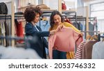 Small photo of Young Female Customer Shopping in Clothing Store, Retail Sales Associate Helps with Advice. Diverse People in Fashionable Shop, Choosing Stylish Clothes, Colorful Brand with Sustainable Designs