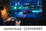 Small photo of Close Up on Man's Hands at Home, Sitting on a Couch in Stylish Loft Apartment and Playing Arcade Car Video Games on Console. Male Using Controller to Play Street Racing Drift Simulator.