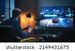 Small photo of Young Man Spending Time at Home, Sitting on a Couch in Stylish Loft Apartment and Playing Arcade Car Video Games on Console. Male Using Controller to Play Street Racing Drift Simulator.