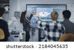 Small photo of Caucasian Student Girl Raise Her Hand and Asking Teacher Standing Near the Big Screen. Teenagers Studying Robotic Arm at the Lesson In Modern University of Technology. Machine Learning Concept